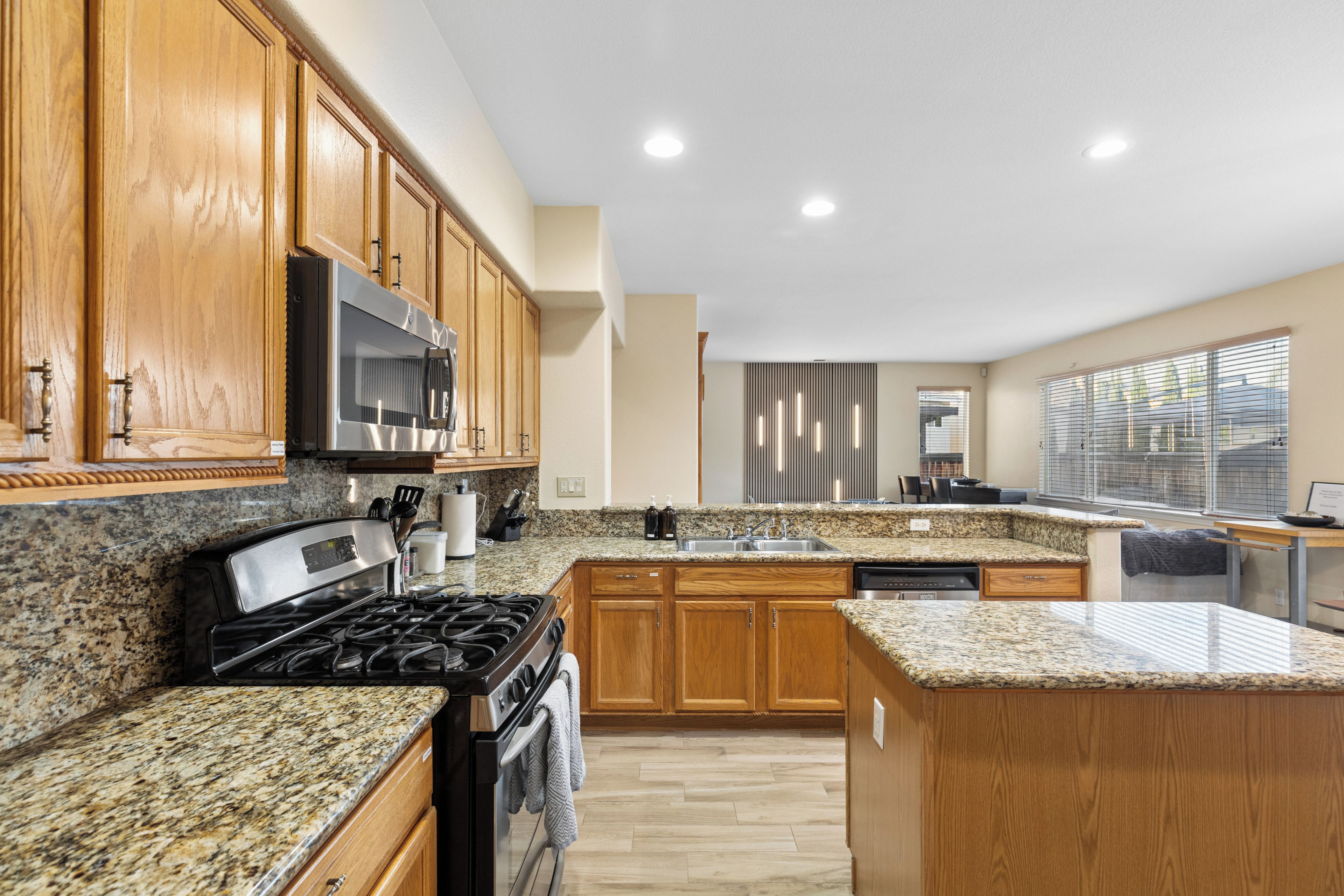A modern kitchen with granite countertops, wooden cabinets, stainless steel appliances, and a built-in dishwasher.
