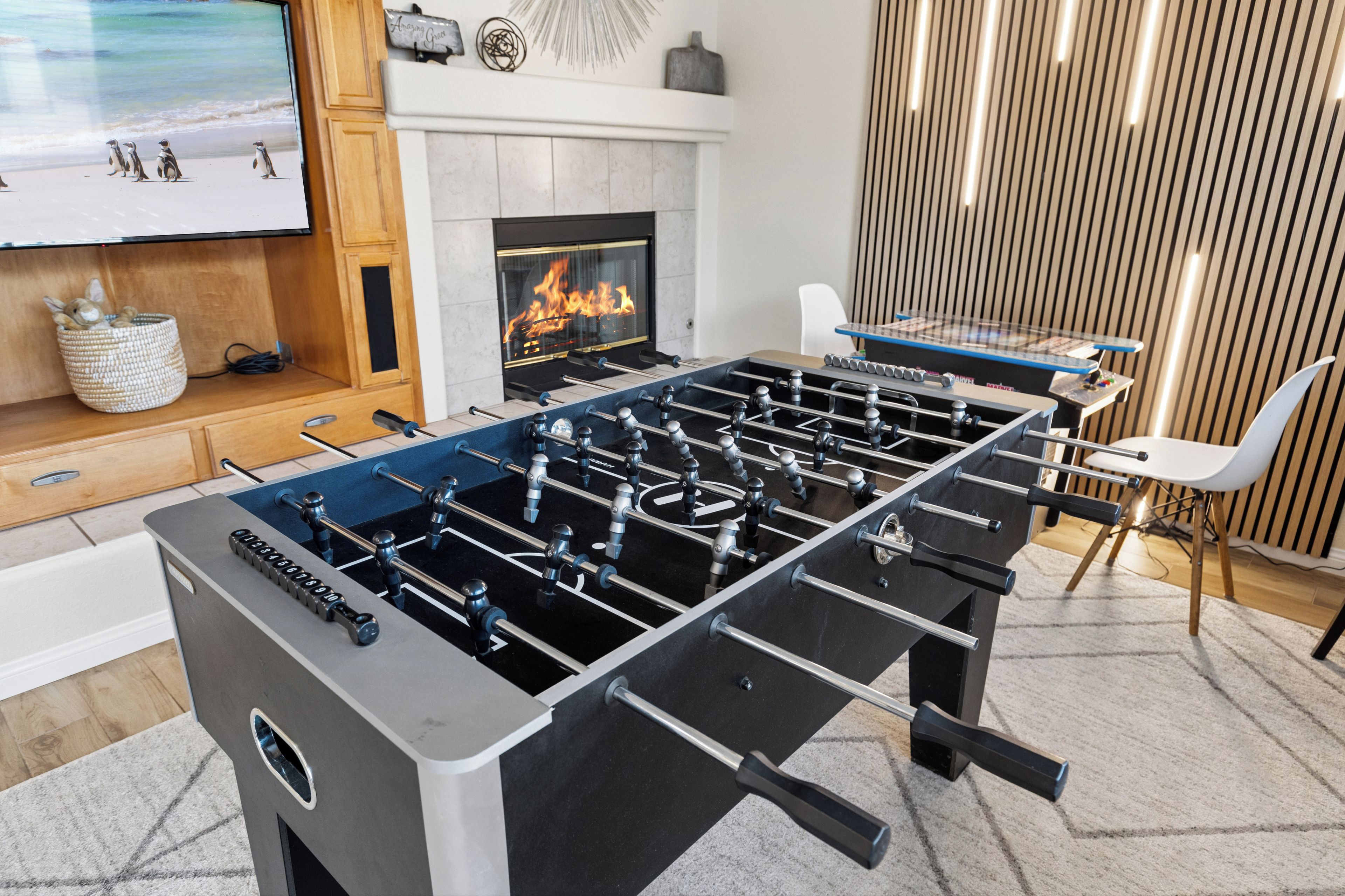 A modern living room with a foosball table, a fireplace, and a television displaying penguins.