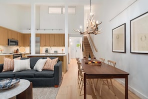 Eine moderne Küche mit Holzschränken, ein Essbereich mit Holztisch und -stühlen sowie eine Treppe, die in eine obere Ebene führt.