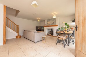 A modern living room with a sofa, a dining table with chairs, a small round table, and a staircase. - Charming Countryside Barn | Rural Shropshire - Pass the Keys (Newport)