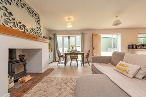A living room with a sofa, a fireplace, a dining area with a table and chairs, and a large window. - Charming Countryside Barn | Rural Shropshire - Pass the Keys (Newport)