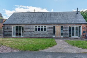 A log cabin with a stone foundation, large glass doors, and a chimney. - Charming Countryside Barn | Rural Shropshire - Pass the Keys (Newport)
