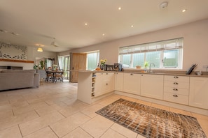 A modern kitchen with white cabinets, a dining area with a grey sofa, and a patterned rug. - Charming Countryside Barn | Rural Shropshire - Pass the Keys (Newport)