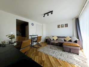 Ein Wohnzimmer mit einer Couch, Sesseln, einem Couchtisch, einem Teppich und einem Essbereich mit Tisch und Stühlen.