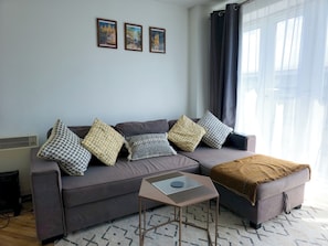 Ein Wohnzimmer mit grauem Sofa, gemusterten Kissen, einem kleinen Tisch und drei gerahmten Bildern an der Wand.