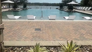 Ein Swimmingpool mit Liegestühlen, einer Ziegelterrasse und Blick auf ein weiter entferntes Gewässer.