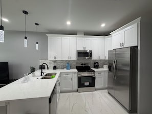 Een moderne keuken met witte kasten, roestvrijstalen apparatuur, een marmeren aanrecht en hanglampen.