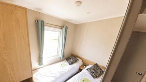 Una habitación pequeña con dos camas, una ventana con cortinas y un armario de madera.