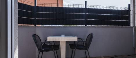 Un petit espace extérieur aménagé avec une table et deux chaises, une clôture en métal noir et un bâtiment en arrière-plan.