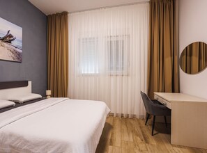 A hotel room with a bed, a desk, a chair, a lamp, and a window with curtains. - Modern Apartment Near The Sea (Podstrana)