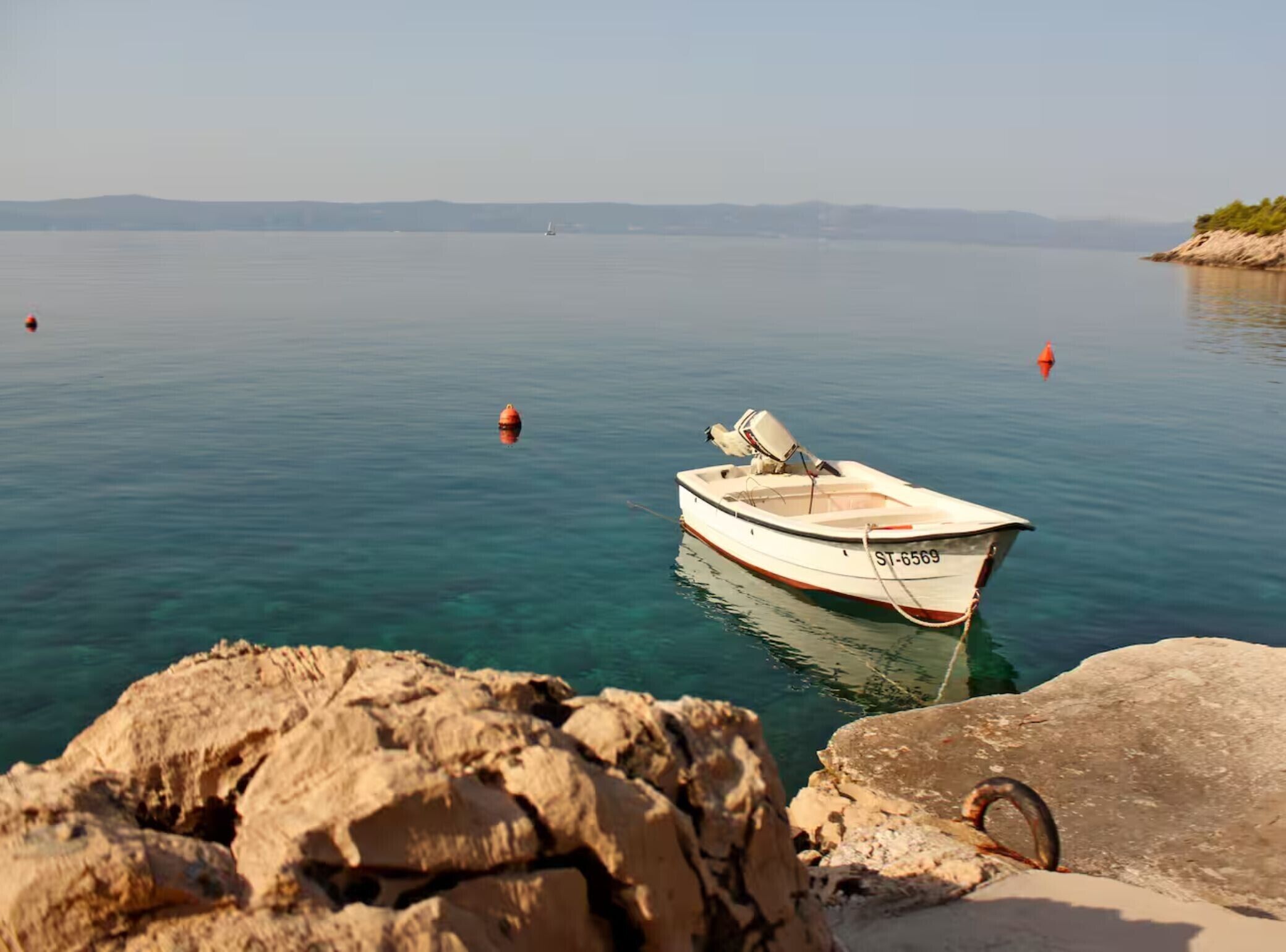 A boat named ST-6569 anchored near rocky shores with calm water and distant land.