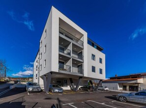 A modern multi-story building with balconies, parking spaces, and a clear blue sky.