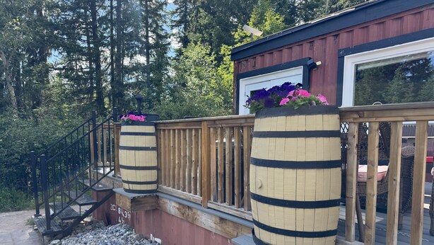 A wooden deck with a railing, a stone pathway, and a wooden structure with barrels. - Unique Container home. 10 min from town. Stunning Mountain Views! (Golden)