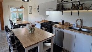 A modern kitchen with a wooden table, black chairs, a stove, oven, dishwasher, and a sink. - Unique Container home. 10 min from town. Stunning Mountain Views! (Golden)