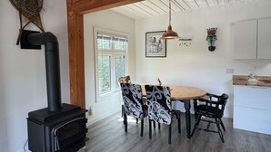 A kitchen with a black stove, wooden beams, a dining table with patterned chairs, and a hanging pendant light. - Unique Container home. 10 min from town. Stunning Mountain Views! (Golden)