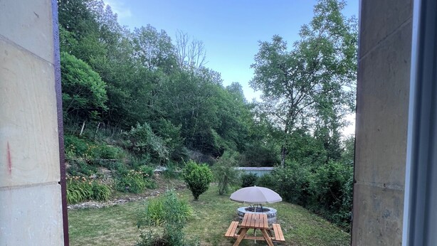 A view through a doorway into a backyard with a wooden table, an umbrella, and a blue chair.