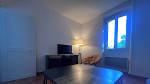 A room with a dining table, a television, a lamp, a chair, and a window.