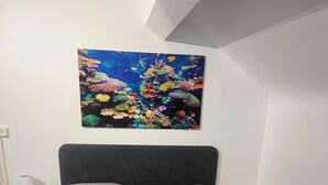 A bedroom with a bed, two pillows, a nightstand, a lamp, and a wall-mounted painting of a coral reef.