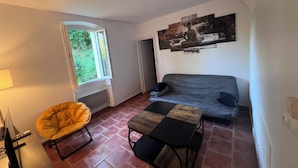 A room with a sofa, a table, a chair, a window, and a painting on the wall.
