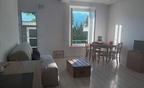 Ein modernes Wohnzimmer mit einer Couch, einer Holzkiste, einem Esstisch mit Stühlen und einem Fernseher.