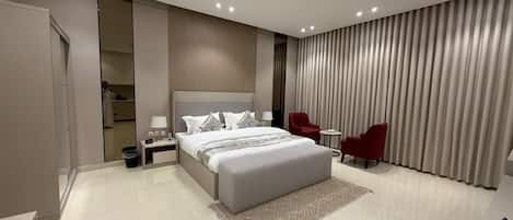 A modern hotel room with a large bed, a red chair, a small table, and a wardrobe.