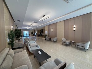 A spacious lobby with a long reception desk, several seating areas with sofas and chairs, and a large plant. - valia (Alkharj)