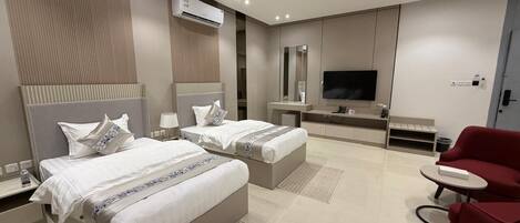 A modern hotel room with two beds, a TV, a red armchair, and a small table.