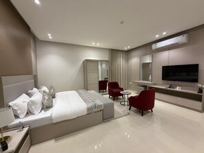 A modern hotel room with a large bed, a TV, a desk, and a seating area. - valia (Alkharj)
