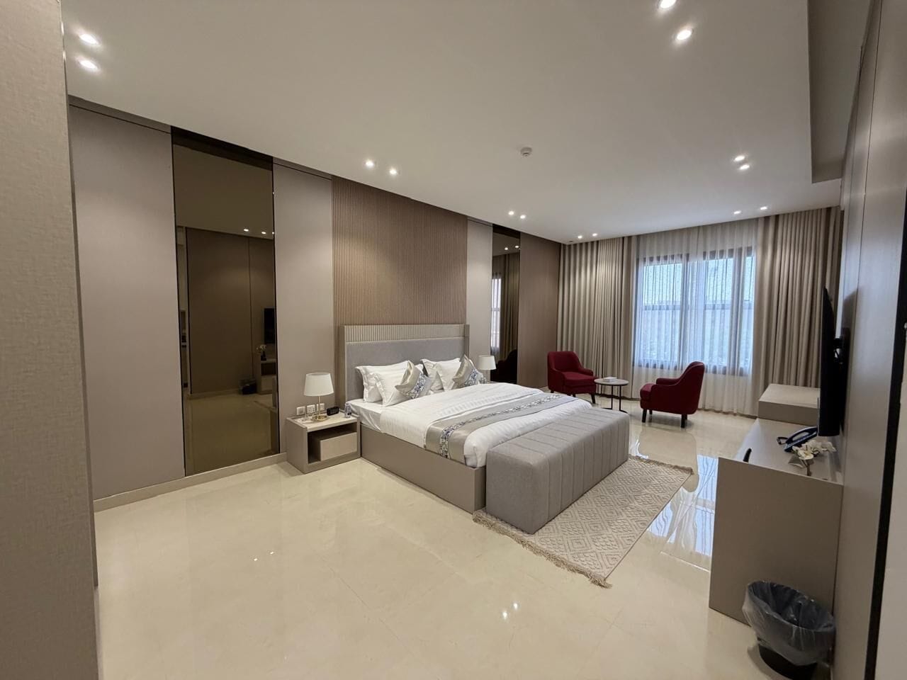 A modern hotel room with a large bed, a desk, a chair, and a TV.