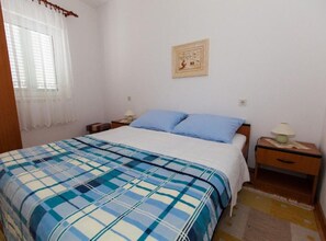 Ein Schlafzimmer mit einem Bett, zwei Nachttischen, einem Fenster mit Vorhängen und einem Wandbild.