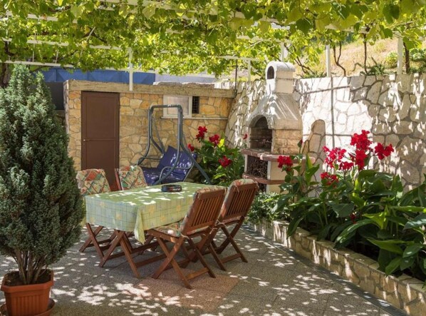 Eine Terrasse im Freien mit Tisch, Stühlen, einem Steinofen und Topfpflanzen.