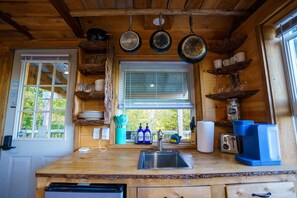 A wooden cabin kitchen with a sink, coffee maker, and hanging pots.