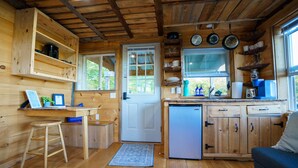 A compact wooden cabin with a kitchenette, a single door, and a small stool. - Romantic Private Cabin Getaway with Hot Tub and Scenic Views (Deansboro)