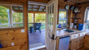 A wooden cabin with a kitchen, a dining area with a grill, and a view of the surrounding forest. - Romantic Private Cabin Getaway with Hot Tub and Scenic Views (Deansboro)