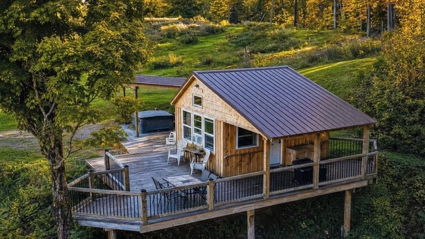 A wooden cabin with a deck, surrounded by greenery. - Romantic Private Cabin Getaway with Hot Tub and Scenic Views (Deansboro)