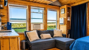 A cozy cabin with a sofa, a small kitchen area, and a view of the outdoors. - Romantic Private Cabin Getaway with Hot Tub and Scenic Views (Deansboro)