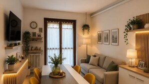 A modern living room with a sofa, a dining table with chairs, a TV mounted on the wall, and a kitchen area with cabinets and a countertop. - Frenk House above Varenna (Lombardia)