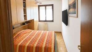A bedroom with a bed, a radiator, a window, a TV, and a painting on the wall. - Frenk House above Varenna (Lombardia)
