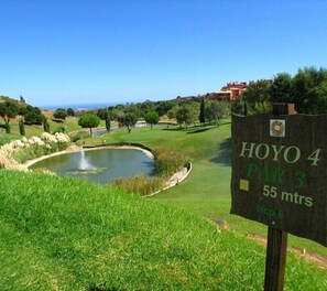 Un panneau indiquant un trou de golf avec les inscriptions « HOYO 4 PAR 3 55 mètres » et « Hop 6 », qui précisent le numéro du trou et la distance.