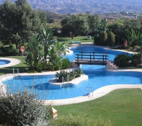 Piscina com uma ponte, rodeada por vegetação e uma paisagem acidentada.