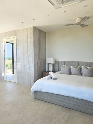 Een moderne hotelkamer met een groot bed, een plafondventilator, een nachtkastje en uitzicht door een geopende deur.
