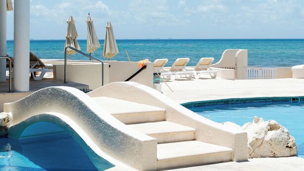 Ein Poolbereich mit Liegestühlen und Sonnenschirmen, mit freiem Blick auf das Meer und einem Gebäudebau.