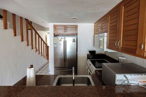 Eine Küche mit Holzausstattung, einem Edelstahl-Kühlschrank, einer Mikrowelle und einem Spülbecken.