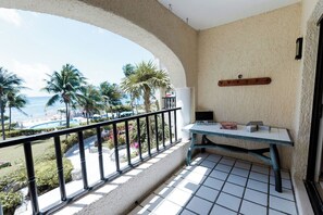Ein Balkon mit Blick auf den Strand, ein Tisch mit einer Kiste und ein an der Wand befestigtes Regal.