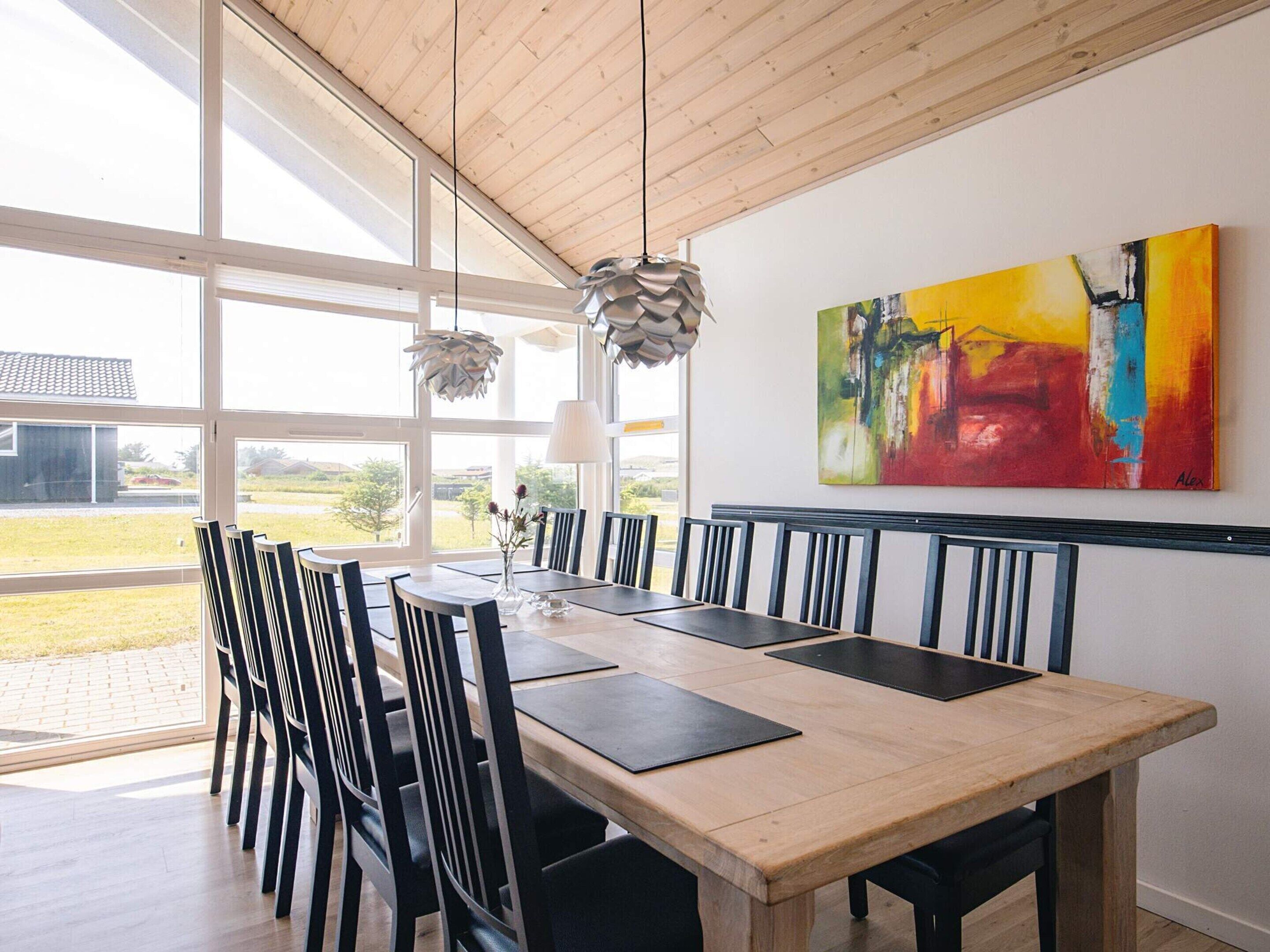 Un coin repas avec une table en bois, des chaises noires et une grande fenêtre donnant sur l’extérieur.