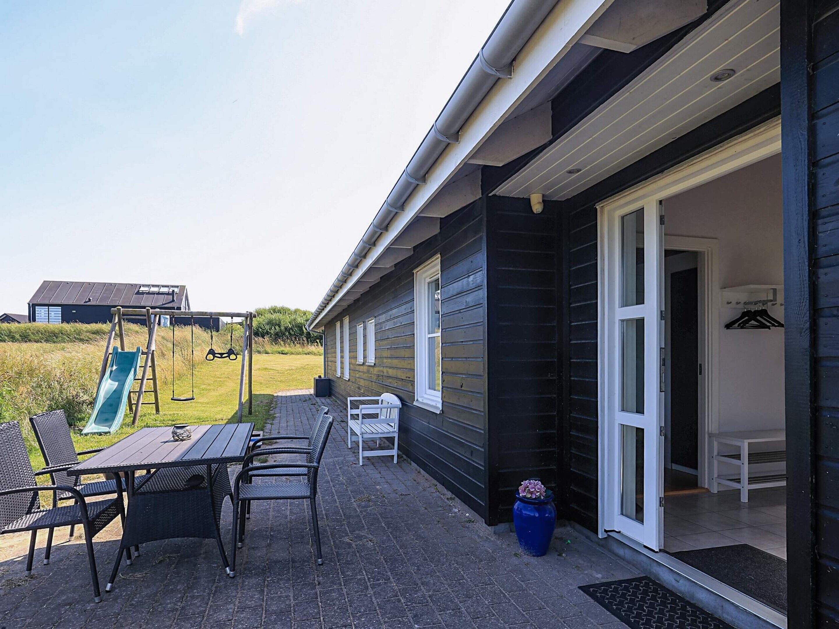 A patio with outdoor furniture, a swing set, and a sliding door leading to a room.
