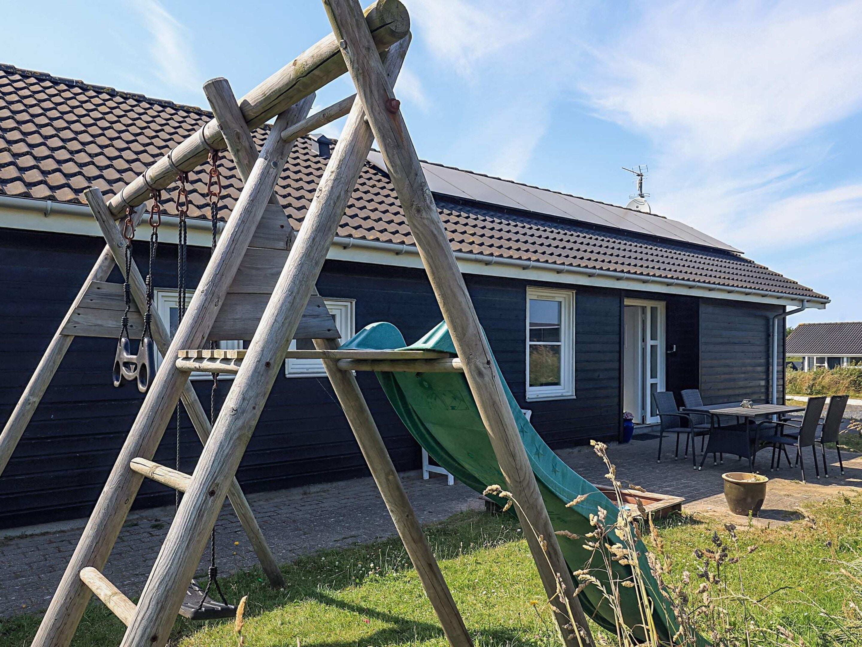 A house with a green slide, a wooden ladder, and a patio with outdoor furniture.