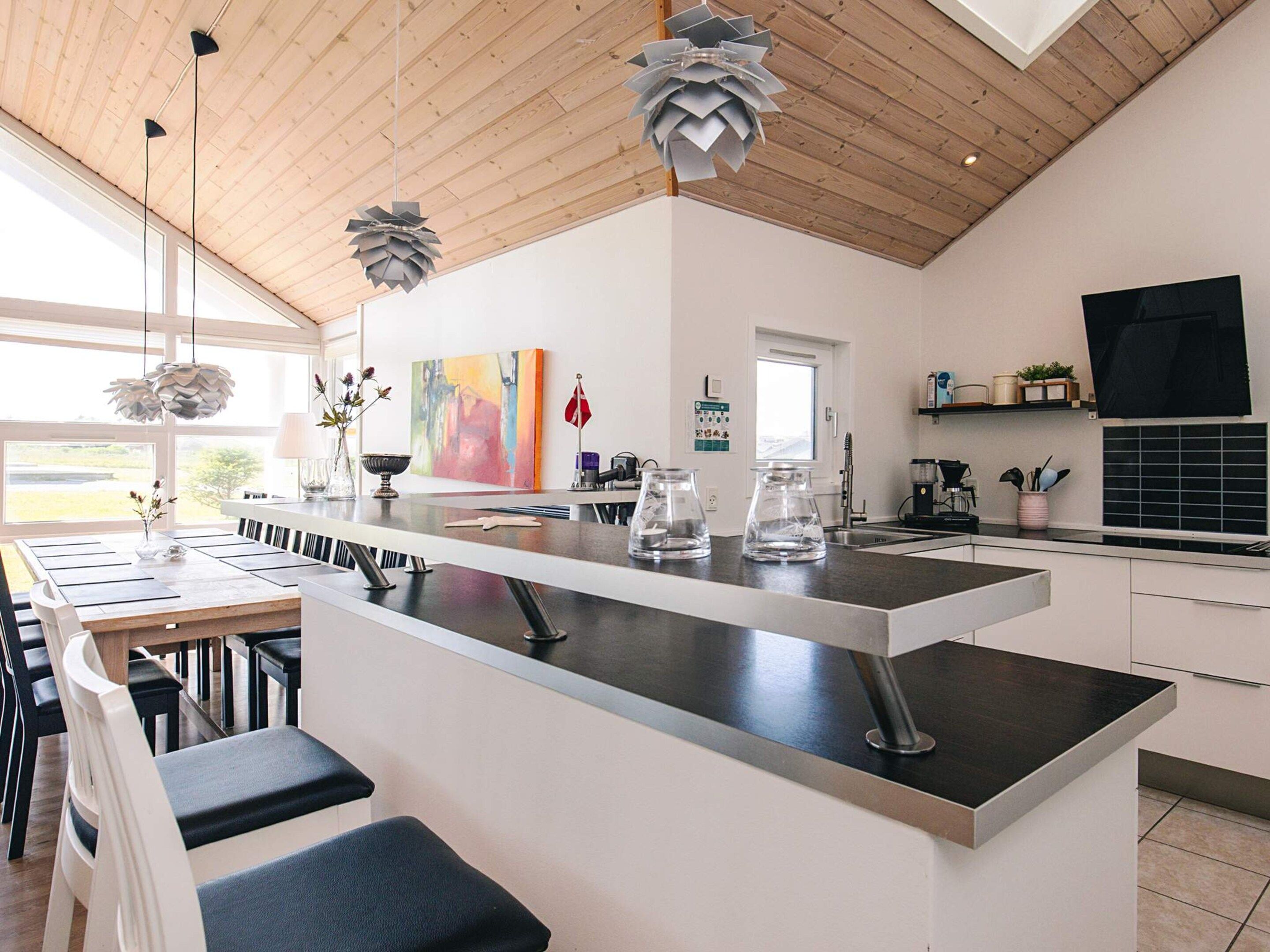 A modern kitchen with a central island, stainless steel appliances, and a wooden ceiling.