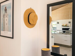 A framed artwork of a tower, a woven hat on the wall, and a kitchen area with cabinets and a countertop. - 5 Star Holiday Home in Lokken (Lokken)