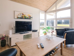 A modern living room with a flat-screen TV, a wooden coffee table, a black leather sofa, and a large window offering a view of the outdoors. - 5 Star Holiday Home in Lokken (Lokken)